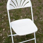 A white folding chair positioned on the ground, showcasing its simple and functional design in an outdoor setting.