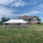 A beautifully arranged wedding tent in a serene field, adorned with elegant decorations and surrounded by lush greenery.